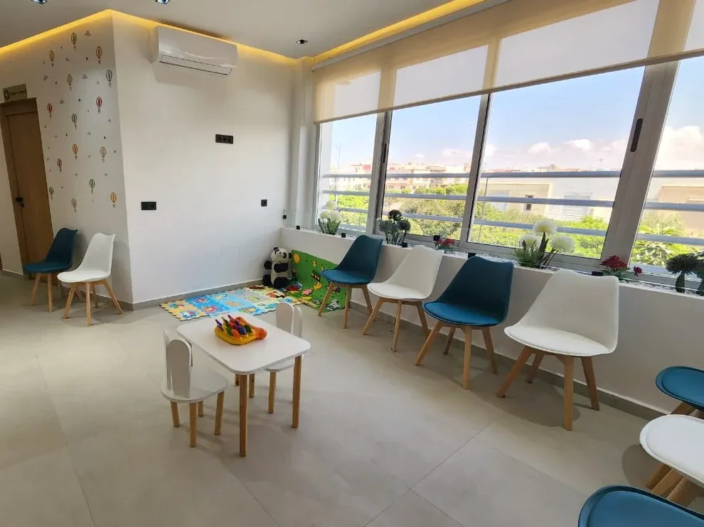 Espace d’attente lumineux : coin jeux avec tapis et peluche, petite table pour enfants et chaises face aux baies vitrées